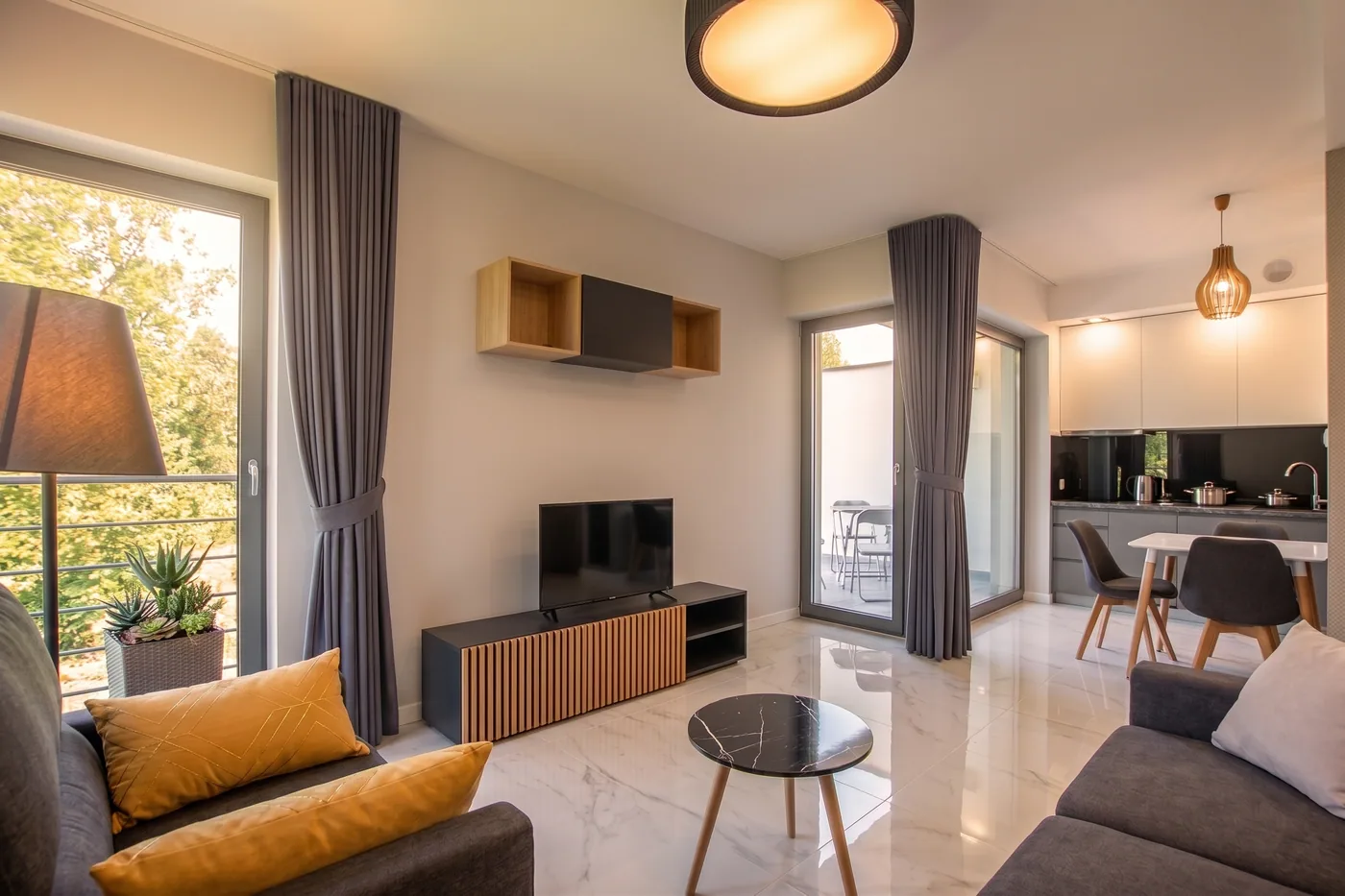 Apartamenty Szmaragdowa 10 — salon z TV i wyjściem na balkon oraz aneksem kuchennym