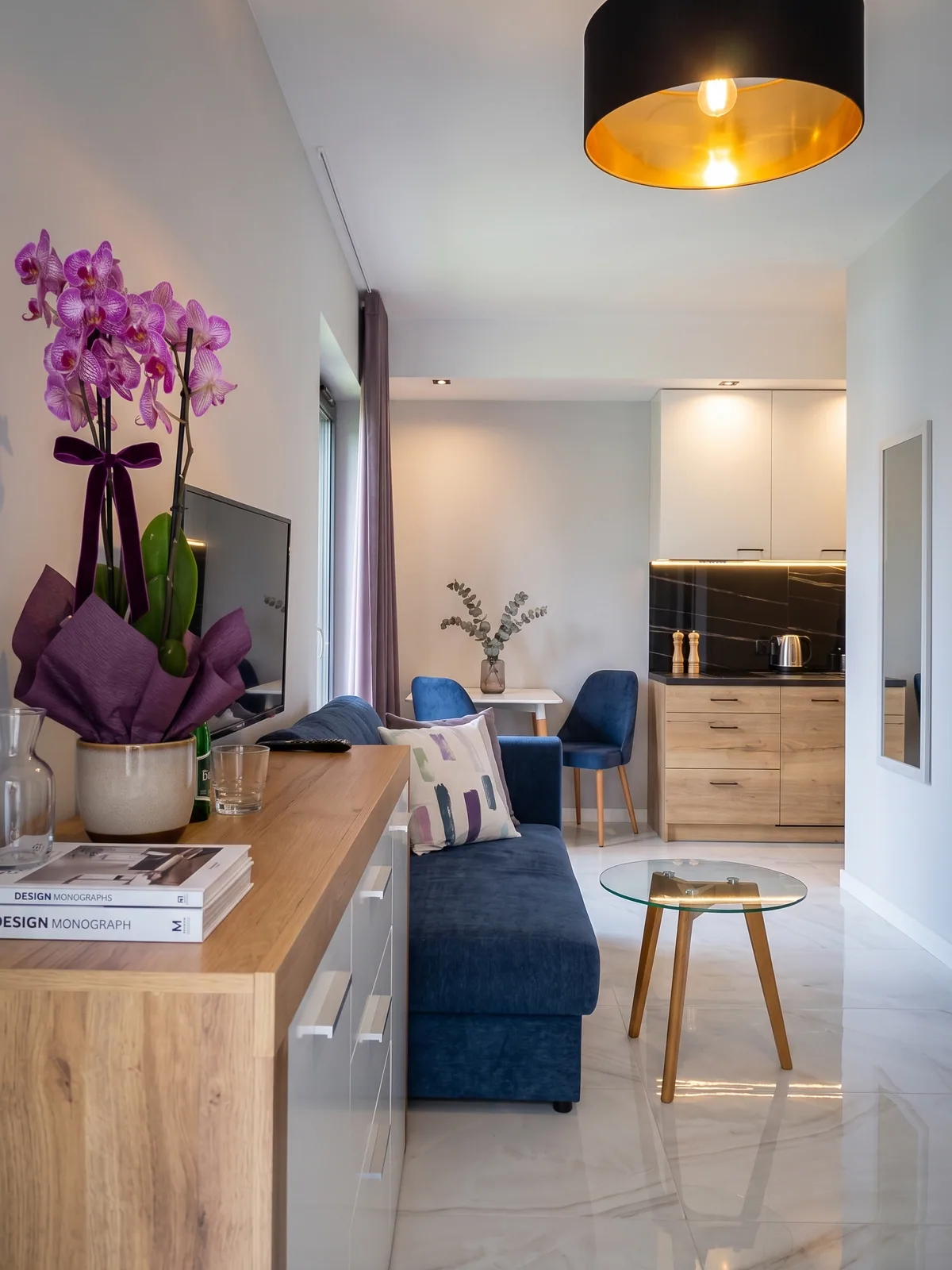 Apartamenty Szmaragdowa 10 — salon z rozkładaną sofą, aneksem kuchennym i kącikiem jadalnym