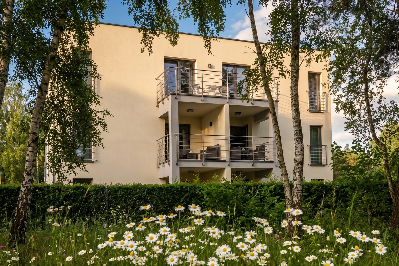 Apartamenty Szmaragdowa 10 — budynek wśród brzóz, łąka z rumiankami