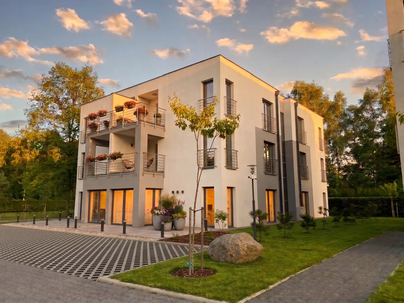 Apartamenty Szmaragdowa 10 — budynek w blasku zachodzącego słońca, kwiaty na balkonach