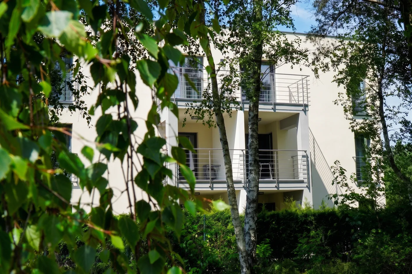 Apartamenty Szmaragdowa 10 — balkony widziane przez gałęzie brzóz